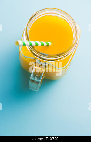 Pichet de jus d'orange. Jus en verre avec paille rayé sur fond bleu. Vue d'en haut. Banque D'Images