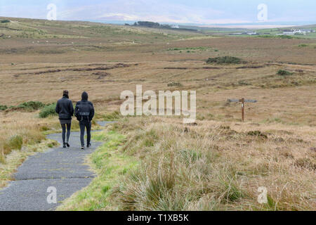 Deux touristes, l'homme et de la femme, de marcher à travers bogland en Irlande sur un sentier en pierre sur une journée d'automne dans le Parc National de Ballycroy, Comté de Mayo. Banque D'Images