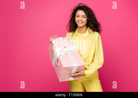 Belle accolade african american woman holding boîte cadeau rose avec ruban de satin blanc isolé sur fond rouge foncé Banque D'Images