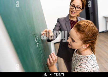Élève écrit sur tableau noir avec une craie au cours de cours de mathématiques Banque D'Images