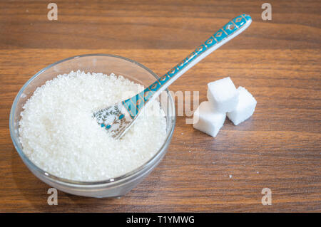 Sucre blanc conservé dans un bol en verre avec une cuillère. Quelques morceaux de sucre conservés sur un plancher en bois Banque D'Images