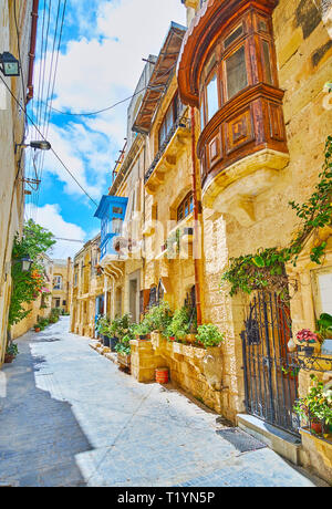 La rue étroite de la vieille ville avec des maisons typiquement maltais, construit de calcaire, d'un balcon en bois coloré et nombreuses fleurs en pots, Ra Banque D'Images