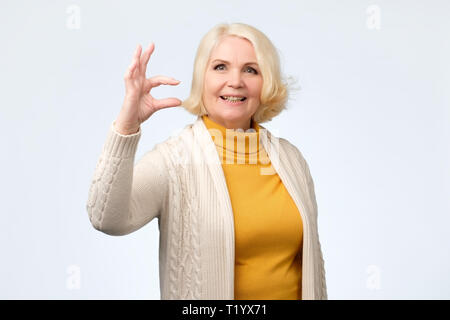 Belle senior woman smiling et montrant des signes de petite taille avec des doigts. mesurer le concept Banque D'Images