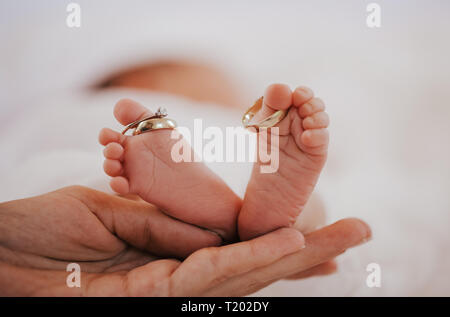 Close up baby avec les anneaux de mariage sur les gros orteils. Tenir la main de la mère les pieds. Banque D'Images