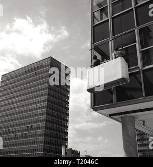 Années 1960, historiques, deux hommes de vitres debout dans un navire ou suspendus au plafond, nettoyer les fenêtres d'un immeuble de bureaux moderne de haute élévation, Londres, Angleterre, Royaume-Uni. Banque D'Images