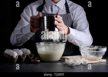 Le tamisage de la farine dans un bol. man cooking pie concept de dessert. Banque D'Images