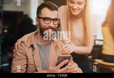 Close up et cut voir d'un homme barbu en veste assis dans un café à la table et tenir un téléphone dans sa main. La jeune fille se trouve à côté de lui un Banque D'Images