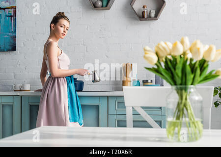 Portrait de jeune femme à préparer le café dans la cuisine près de cezve table avec bouquet de tulipes en pot Banque D'Images