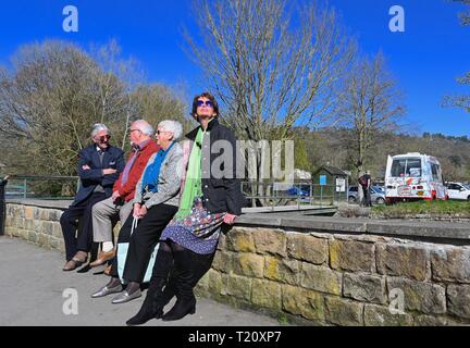 Quatre personnes s'asseoir sur un mur appréciant les soleil du printemps par la rivière Wye de Bakewell, Derbyshire Banque D'Images