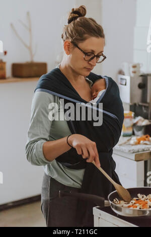 Mère avec bébé en porte-bébé la cuisson Banque D'Images