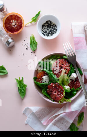 Salade fraîche de printemps avec l'orange sanguine, la laitue, les épinards et les graines de sésame sur fond rose. Vue d'en haut. Selective focus Banque D'Images