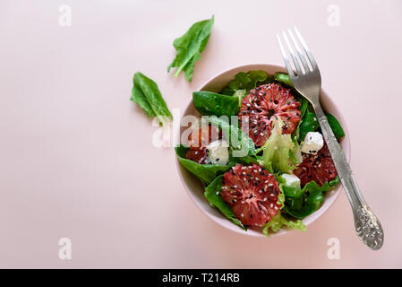Salade fraîche de printemps avec l'orange sanguine, la laitue, les épinards et les graines de sésame sur fond rose. Vue d'en haut. Selective focus Banque D'Images