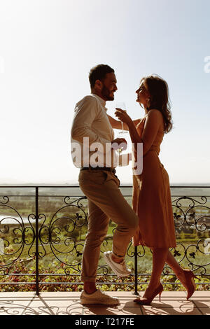Couple romantique sur une date de passer du temps ensemble holding wine. Smiling couple parler et à d'autres à chaque comité permanent en balcon. Banque D'Images