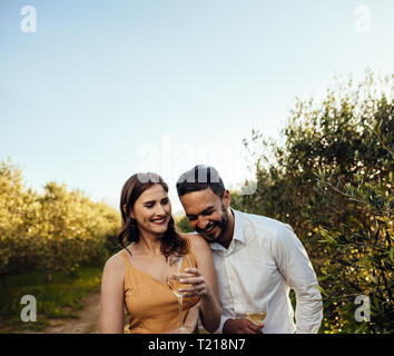 Couple in love rire ensemble et de boire le vin blanc tout en marchant dans un vignoble. Couple heureux sur un vin à une date ferme de vin. Banque D'Images