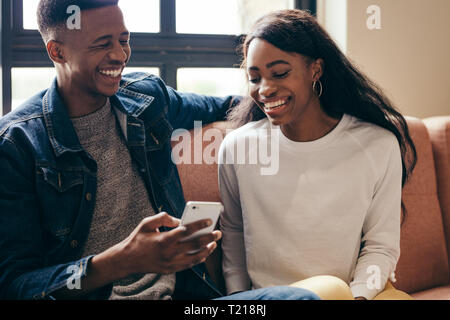 Deux étudiants américains africains using cell phone on campus. Heureux jeune homme et femme assise sur le canapé avec un téléphone intelligent. Banque D'Images