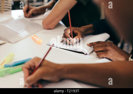 Cropped shot d'étudiants prennent des notes assis à table dans le collège. L'accent des mains des garçons et filles écrit dans leurs livres. Banque D'Images