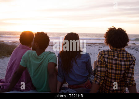 Groupe d'amis assis sur la plage et à la mer à Banque D'Images