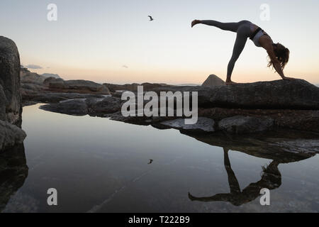 Woman doing yoga on rock at beach Banque D'Images