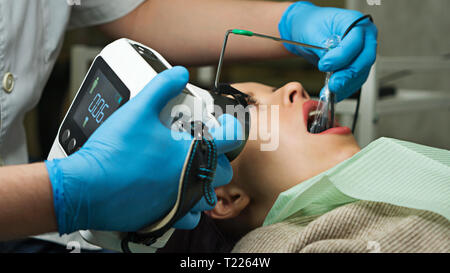 Dentiste vérifie l'épaisseur de l'émail des dents à l'aide de rayons-x portable. Jeune fille avec la bouche ouverte. Des dents blanches. Dentiste mains libre. Clinique dentaire. Banque D'Images