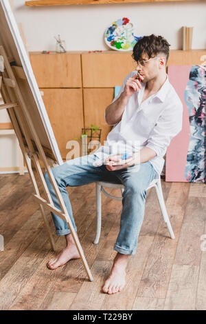 Artiste beau en chemise blanche et un jean bleu à la recherche de toile sur chevalet Banque D'Images