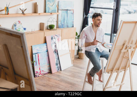 Portrait de l'artiste joyeux assis sur la chaise haute en toile avec chevalet Banque D'Images