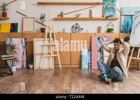 De l'artiste avec les jambes croisées et les mains sur la tête en peinture studio Banque D'Images