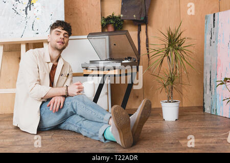 Beau holding Coffee cup and looking at camera, assise près de vinyl record player Banque D'Images