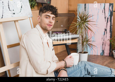 Artiste beau holding Coffee cup alors qu'il était assis près de vinyl record player Banque D'Images