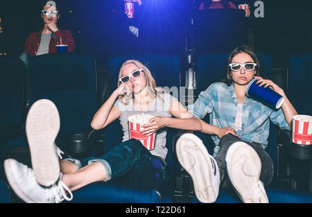 Cool et décontracté fille sont assis dans une rangée avant et regarder la vidéo. Ils ont mis leurs jambes. Ils ne sont d'ailleurs maintenant la tête avec les mains. Un garçon Banque D'Images