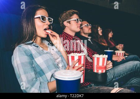 Les gens sont concentrés et sérieux regarder la vidéo. Ils sont assis dans une ligne. Fille brune a un panier de popcron et de le manger. Les autres personnes Banque D'Images