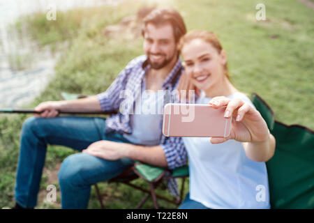 Girl prend des selfies elle-même et son mari. Ils sont à la recherche de téléphone et de sourire. Guy est maintenant la fin des poissons. Les gens sont assis dans fol Banque D'Images