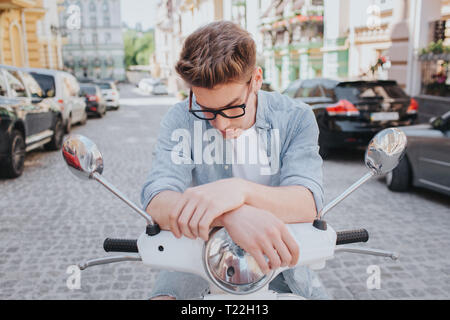 Beau mec est assis sur la moto et à la recherche vers le bas. Il porte des lunettes. L'homme est grave Banque D'Images