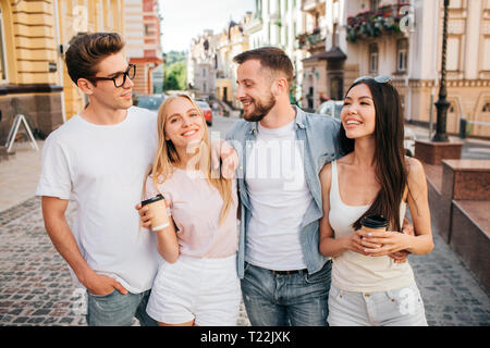 Une photo de belles personnes debout ensemble et poser. Fille blonde sourit à la caméra et la tenue de tasse de café. Jeune chinoise est à la recherche de guy Banque D'Images