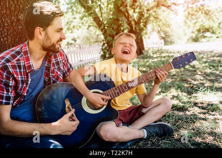 Joyeux et convaincu jeune garçon est tenue de la guitare et jouer sur elle. Il chante et en gardant les yeux fermés. Son père est l'aidant. Il est fier de s Banque D'Images