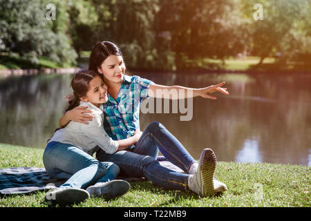 Happy Family est assis ensemble. Femme est serrant sa fille d'une main et pointant vers l'avant. Girl est un petit peu à la mère et à la recherche à Banque D'Images