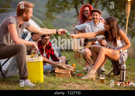 Girl ajouter bouteille de bière au garçon sur le coucher du soleil à forest Banque D'Images