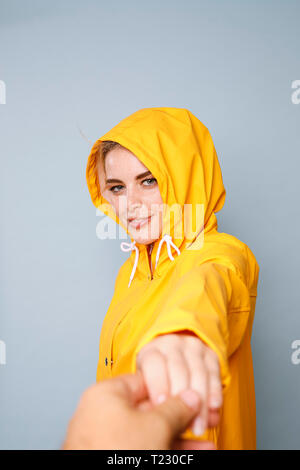 Portrait of smiling young woman wearing manteau de pluie jaune en face de fond bleu holding hands Banque D'Images