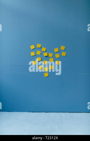 Forme de coeur bleu sur un mur fait de notes adhésives jaunes Banque D'Images