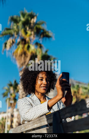 Belle femme assise sur un banc dans la ville, takig photos avec son smartphone Banque D'Images