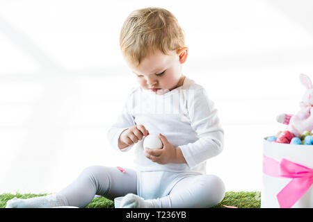 Adorable enfant holding white oeuf de poule en étant assis près de Fort avec des oeufs de Pâques isolated on white Banque D'Images