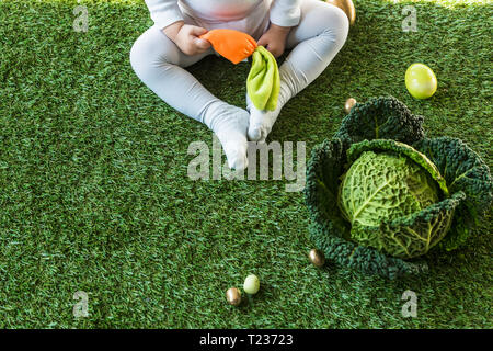 Vue partielle de la holding toy carotte assis près d'œufs de Pâques et chou on Green grass Banque D'Images