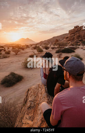 La Namibie, Spitzkoppe, amis assis sur un rocher à regarder le coucher du soleil Banque D'Images