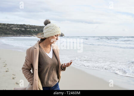 L'Espagne, Minorque, senior woman reading e-book sur la plage en hiver Banque D'Images