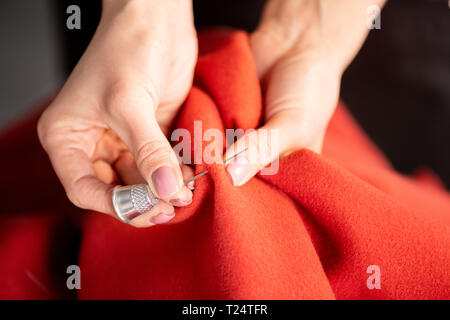 Mains de femme avec dé sur l'index mettre aiguille au travers du textile rouge tout en travaillant plus de coat Banque D'Images