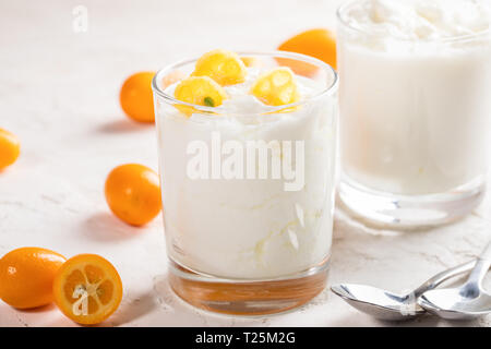 Deux verres avec du yogourt avec tranches de kumquat et deux cuillères sur fond blanc. Banque D'Images