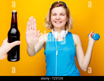 Athletic Girl in headphones avec haltère dans la main en face de la main avec une bouteille de bière. Banque D'Images