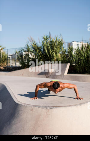 Homme musclé torse nu faisant push-ups dans un skatepark Banque D'Images