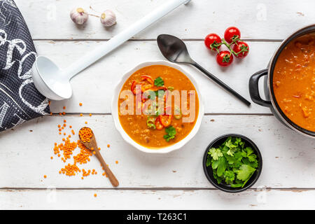 Bol et pot de soupe aux lentilles rouges garnie et ingrédients sur bois blanc Banque D'Images