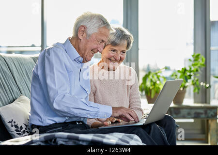 Senior couple sitting on sofa using laptop Banque D'Images