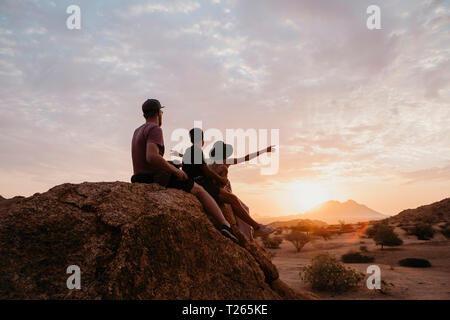 La Namibie, Spitzkoppe, amis assis sur un rocher à regarder le coucher du soleil Banque D'Images